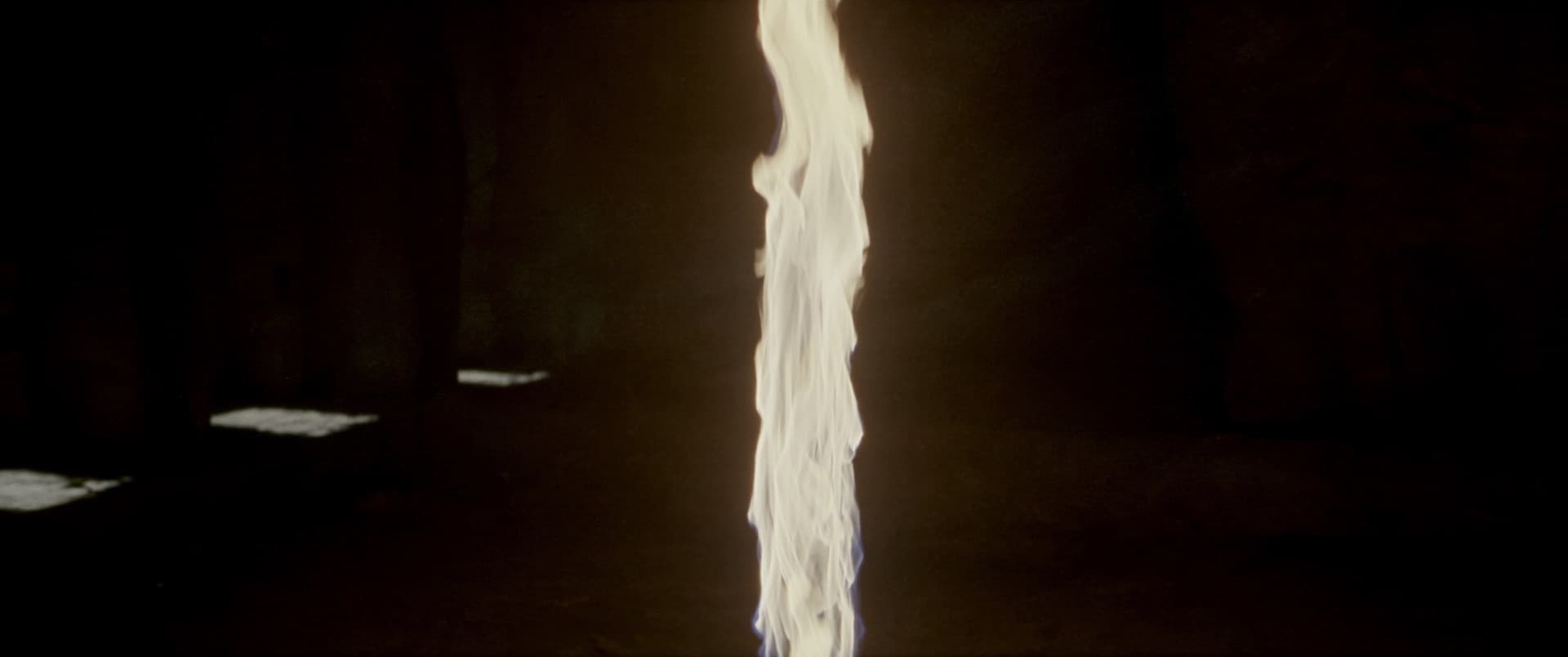 A column of light in an unlit chamber, leaving the frame at the top and at the bottom. Neither end of it is visible, and nothing in the room marks where it begins or stops.